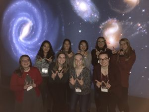 group photo with everyone giving a W sign with their hands, in front of a galaxy-themed backdrop