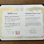 a certificate in Japanese text on the left and English on the right, commemerating Den Hartog's Progress Award